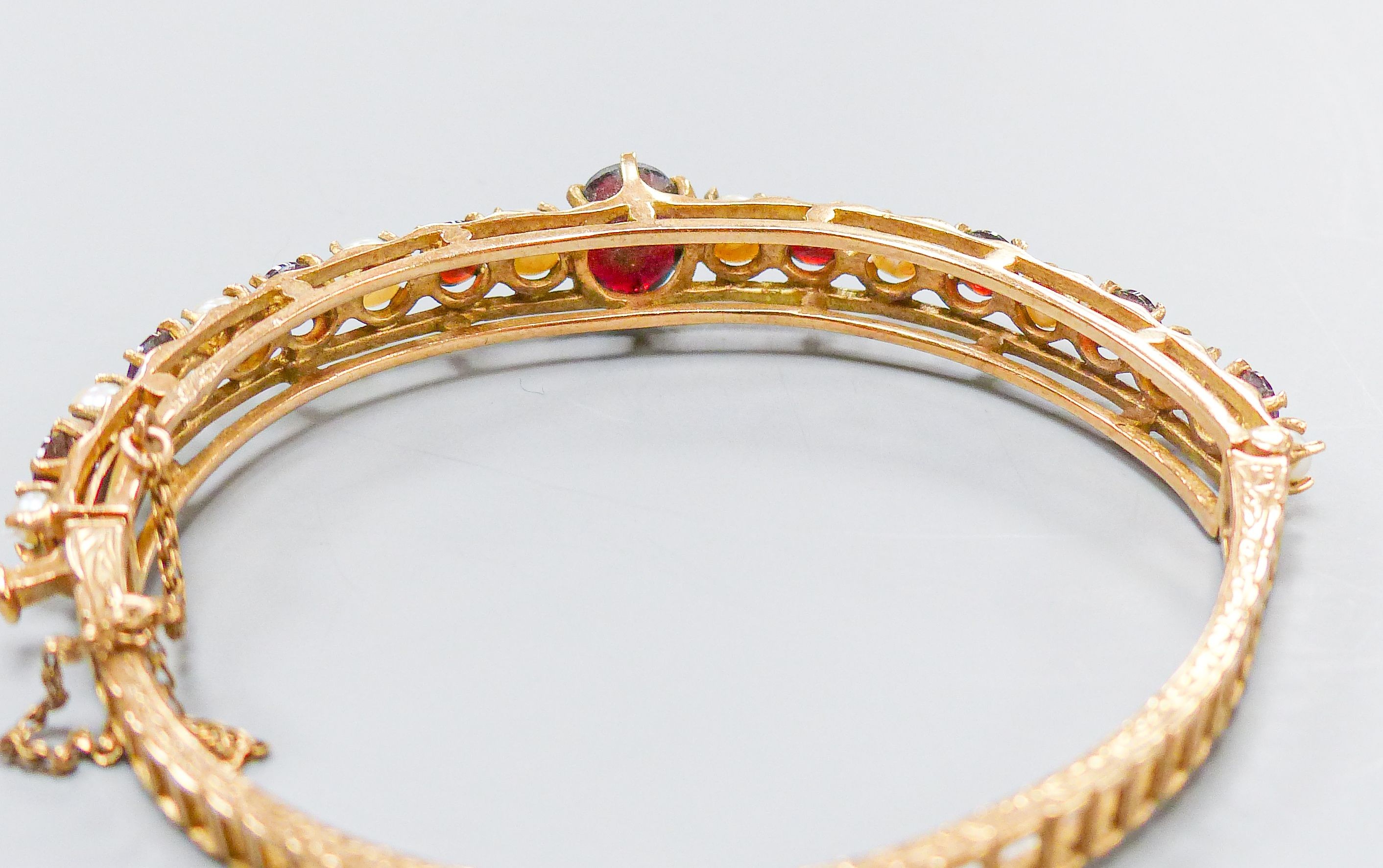 A 9ct gold, garnet and cultured pearl set hinged bracelet, gross weight 16.1 grams.
